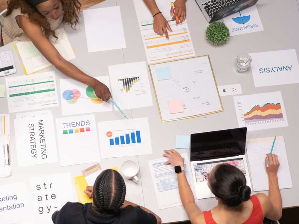 People collaborating at a table with charts, graphs, and documents related to marketing strategies and analysis.