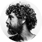 Black and white profile photo of a man with curly hair and a beard, looking to the left against a plain background.