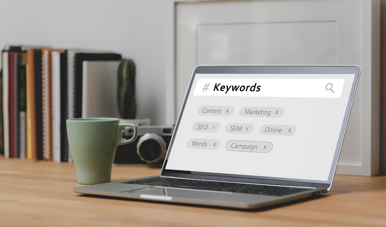 A laptop on a desk displays a search bar labeled "Keywords" with related terms like private label SEO; a green mug and books are in the background.
